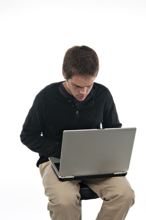 teenage boy sitting on stool looking at laptop on white backgroundの写真素材