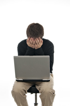 teenager sitting on stool with laptop and his hands covering his face on white backgroundの写真素材