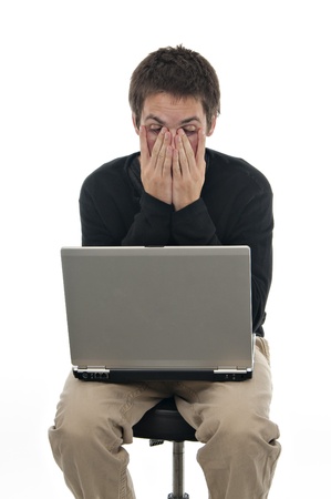 teenager sitting on stool with laptop and his hands covering his face on white backgroundの写真素材