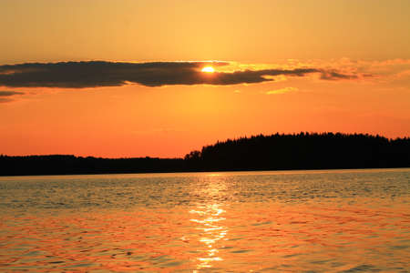 Beautiful sunset at a lake. Sun goes behind a small cloud before falling to the horizonの写真素材
