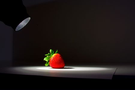 Lucious, ripe, red , juicy strawberry highlighted by a single spotlight against a dark background.の写真素材