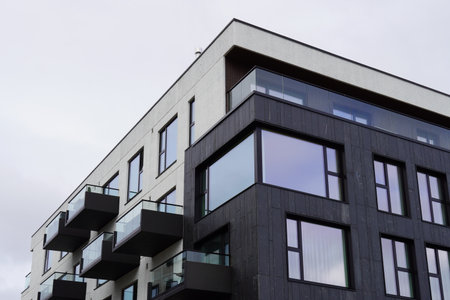 Modern apartment building with balconies and large windows under a cloudy sky in an urban settingの写真素材