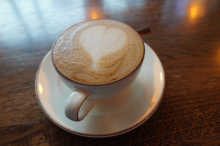 Warm heart-shaped latte art served in a simple white cup on a wooden table