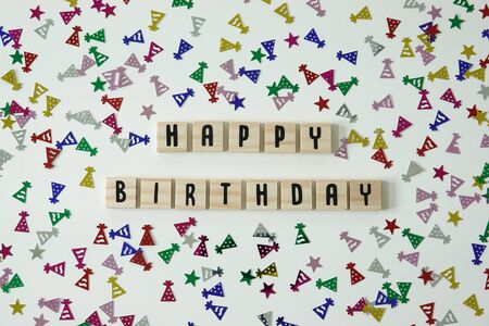 Happy birthday written in wooden letter tiles with confetti birthday hats and stars surrounding it.の写真素材