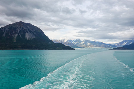 The wake of a cruise ship sailing away from Hubbard Glacier with a view of the glacier and mountains.の写真素材