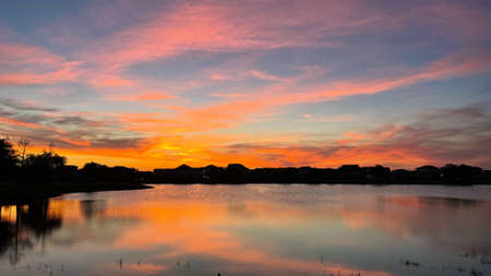 Beautiful pink, orange and blue sunset reflecting on a lake in a suburban neighborhood.の写真素材