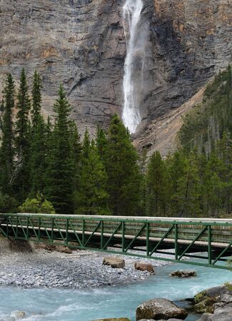 Takakkaw Falls In Yoho National Park With A Wooden Bridge Over Yoho River In The Foregroundの写真素材