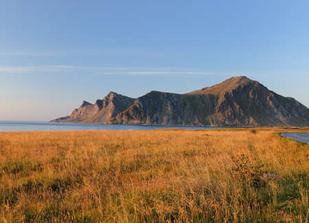 View To The Mountains Of Lofoten Island Flakstadoy In The Late Afternoon Sun On A Sunny Summer Day With A Clear Blue Sky And A Few Cloudsの写真素材