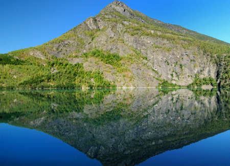 Mountains Reflecting In The Calm Water Of Lake Eidsvatnet Near Skjolden On A Sunny Summer Day With A Clear Blue Skyの写真素材