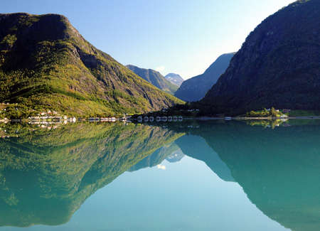Mountains Reflecting In The Calm Water Of The Dalsfjord Near Skjolden On A Sunny Summer Day With A Clear Blue Sky And A Few Cloudsの写真素材