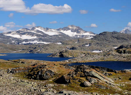 Lakes And Glaciers In The Barren Landscape Of The Icefields Of Jotunheimen National Park On A Sunny Summer Day With A Clear Blue Sky And A Few Cloudsの写真素材