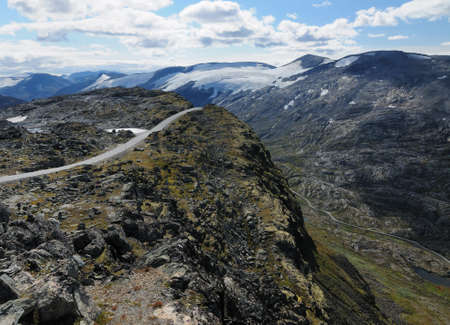 Winding Road From Dalsnibba Into The Barren Valley Surrounded By Glacier Covered Mountains To Geirangerfjord On A Sunny Summer Day With A Clear Blue Sky And A Few Cloudsの写真素材