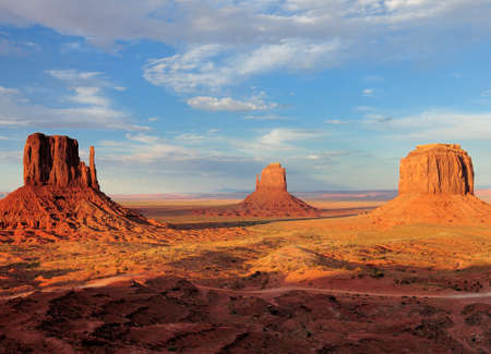 View To The East Mitten Butte, Merrick Butte And West Mitten Butte In The Monument Valley Arizona In The Late Afternoon Sun On A Sunny Summer Day With A Clear Blue Sky And A Few Cloudsの写真素材
