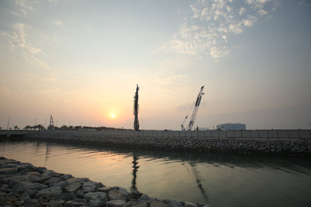 Lakeside construction site with crane and building silhouettes at sunsetの写真素材
