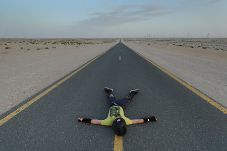 A young woman lying on the road in the middle of the desertの写真素材