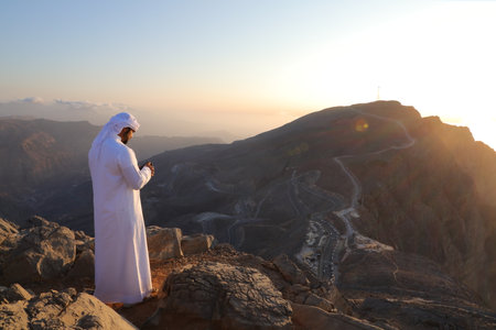 Handsome Arabian man in traditional clothes praying on top of the mountain.の写真素材