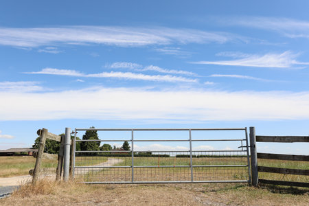 A gate in a rural field under a blue sky with white cloudsの写真素材