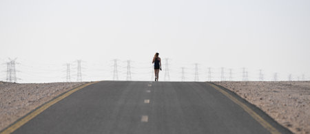 Woman walking on a road in the desert with high voltage towers in the backgroundの写真素材