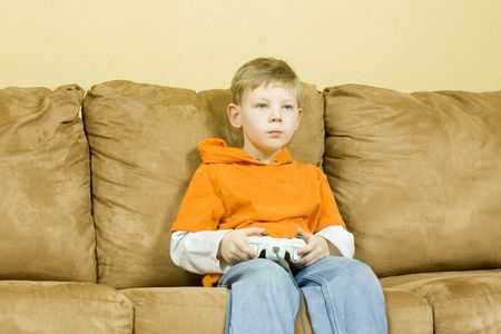 Young boy sitting on couch playing a gameの写真素材