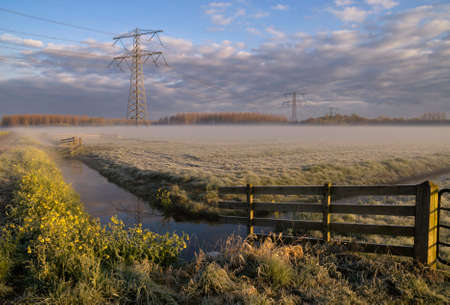 Morning fog above a meadow with electricity pylonsの写真素材