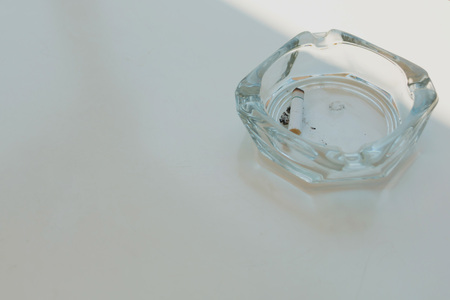 Glass ashtray with one cigarette in it on white table in different light and shade.の写真素材