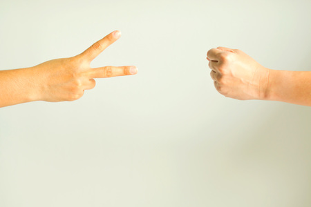 Two hand playing rock paper scissors; one hand showing scissors sign and another hand showing rock sign.の写真素材