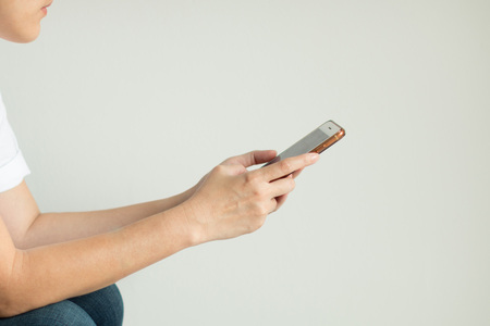 A woman in white T-shirt and jeans is using mobile phone for shopping online and internet banking.の写真素材