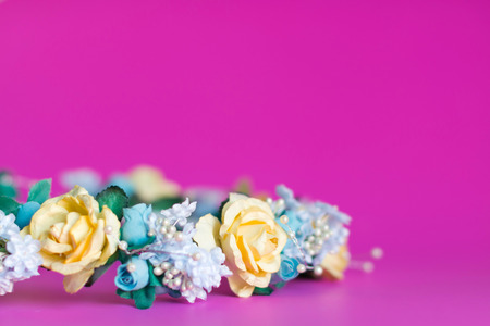 Artificial chaplet (wreath of flowers) of yellow roses and blue flower on pink background.の写真素材