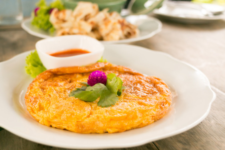 Crab omelet with chilli ketchup served on white plate decorated with pink Globe amaranth flower on wooden table.の写真素材