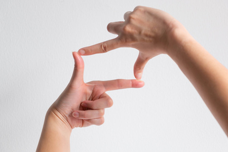 A person using thumb and forefinger of two hand to make a shape of camera frame on white background; concept of make a focus or have an aim.の写真素材