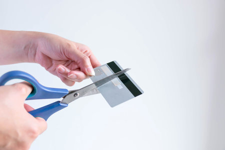 A person is cutting a credit card with blue scissors on white background with copy space; concept of...