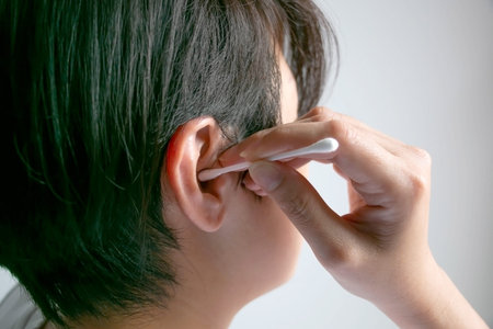 Close-up image  in right side of woman is cleaning her ear with cotton bud; concept of health care and body hygiene.の写真素材