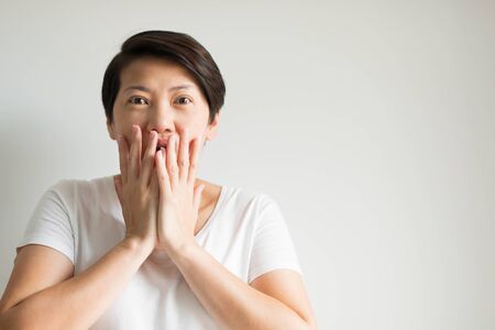 Portrait of a woman uses two hands closing her mouth and looking at the front of her with feeling excited, amazed and happy.の写真素材