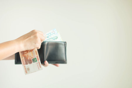 Hand holding a wallet and Russian money in RUB currency; another hand-selecting more banknotes from...