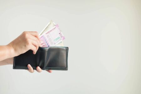 Close-up of hands holding a short wallet and one hand bring out the money in the currency of Rupee or INR; from the wallet to pay for something on white background.の写真素材
