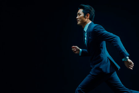 Portrait of a young handsome asian businessman in suit running on black backgroundの素材