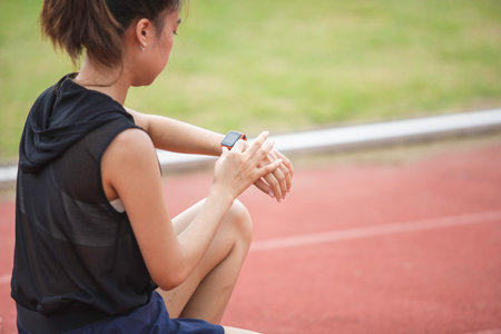 A young woman prepares for her workout, adjusting her fitness gear and setting her smartwatch to track her distance, her eyes gleaming with determination as she readies herself to conquer her fitness goals.の写真素材