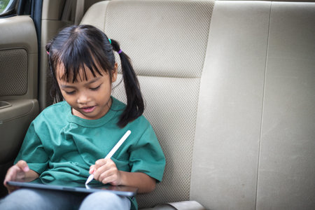The young girl sits in the car, happily drawing on her tablet, eyes sparkling with joy.