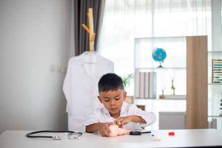A young boy is playing with a doll in a doctor's office. The room is filled with medical equipment, including a stethoscope and a toy doctor's kit. The boy is wearing a white lab coatの写真素材