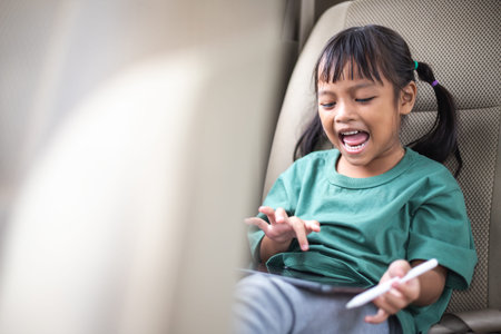 The young girl sits in the car, happily drawing on her tablet, eyes sparkling with joy.