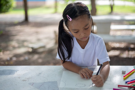 young girls are sitting at a table with markers and coloring books. They are drawing and coloring together, enjoying their time in the park. Concept of fun and creativityの写真素材