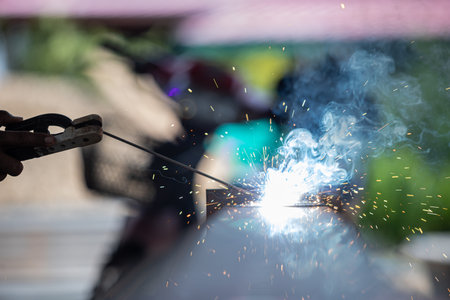 A man is holding a welding torch and sparks are flying. Concept of danger and excitement, as the man is working with a potentially hazardous tool. The sparks and heat from the torch create a dramaticの写真素材