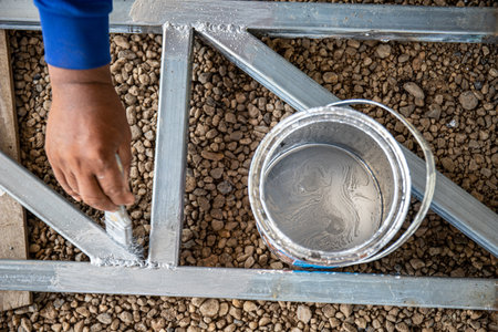 A man is painting a metal structure with a brush. He is wearing a blue shirt and sandalsの写真素材