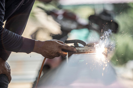 A man is holding a welding torch and sparks are flying. Concept of danger and excitement, as the man is working with a potentially hazardous tool. The sparks and heat from the torch create a dramaticの写真素材