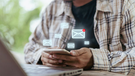 A man is looking at his cell phone with a screen that has a bunch of emails on itの写真素材