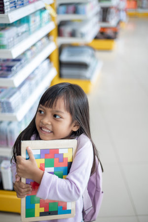 A young girl is holding a puzzle book in a store. She is smiling and she is excited about the puzzle bookの写真素材