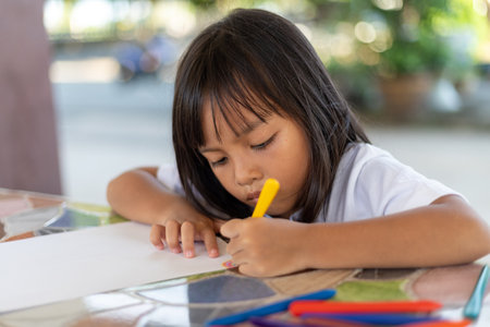 A young girl is drawing on a piece of paper with a marker. She is focused on her drawing and seems to be enjoying herself. Concept of creativity and playfulnessの写真素材