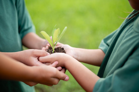 Two children are holding a small plant in their hands. The plant is green and is a seedling. The children seem to be enjoying the experience of planting the seedling and taking care of it, reflecting the importance of instilling environmental values from a young age and fostering a love for nature.の写真素材