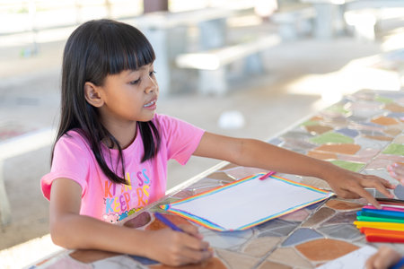 A young girl is drawing on a piece of paper with a marker. She is focused on her drawing and seems to be enjoying herself. Concept of creativity and playfulnessの写真素材