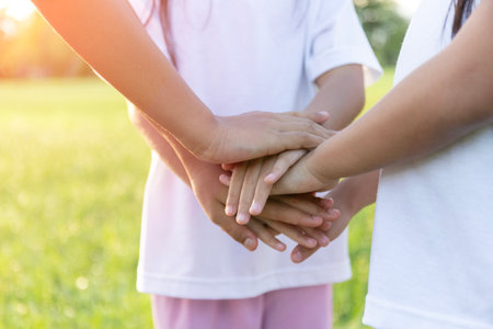Three young girls are holding hands in a circle, with one girl wearing a white shirt. Concept of unity and friendship between the two girlsの写真素材
